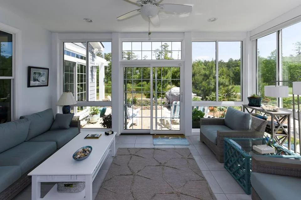 Glass sunroom with white window frames, comfortable seating and garden views